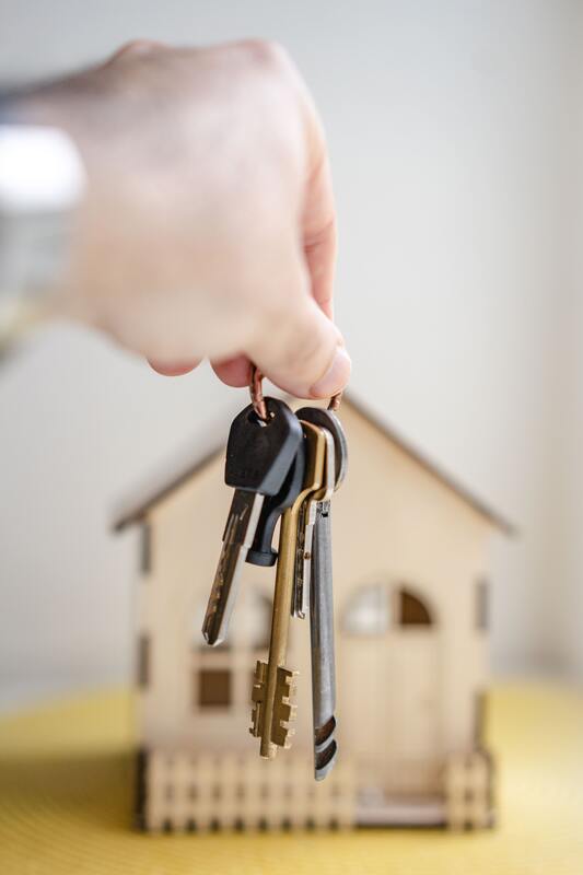 A hand holding keys in front of model house 
