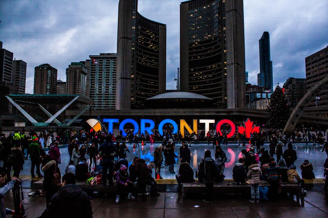 Nathan Phillips square in Toronto Ontario with people ice skating and surrounding the lit Toronto sign and enjoying the evening